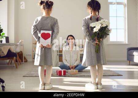 Töchter stehen mit dem Rücken zur Kamera und halten Blumen und eine handgefertigte Postkarte. Stockfoto