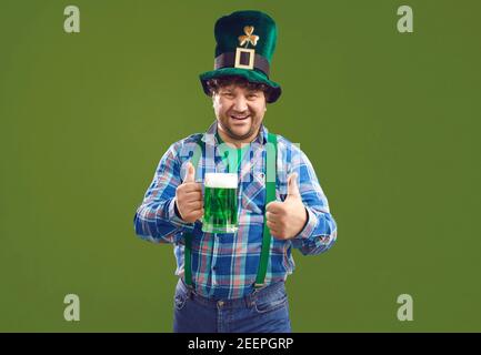Positiver Mann mit grünem Bier zeigt Daumen nach oben während Patrick Tag Stockfoto