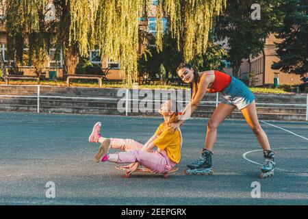 Zwei Teenager-Mädchen, Freunde, die Spaß mit Skate-Board. Ein Mädchen schiebt andere von hinten Stockfoto