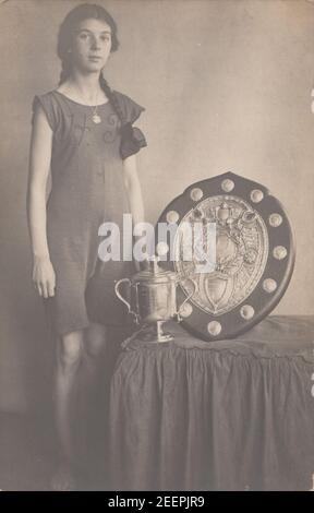 Vintage Anfang 20th Jahrhundert fotografische Postkarte zeigt ein Mädchen stolz zeigt ihre Sporting Trophy und Schild. Stockfoto