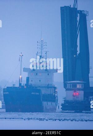 Stralsund, Deutschland. Februar 2021, 16th. Das Frachtschiff Multimar passiert am Abend die offene Ziegelgraben-Brücke zwischen dem Festland und der Insel Rügen. Das eisige Wetter der letzten Tage hat in Mecklenburg-Vorpommern auf den Boddengewässern der Ostsee eine Eisschicht verursacht. Quelle: Jens Büttner/dpa-Zentralbild/dpa/Alamy Live News Stockfoto