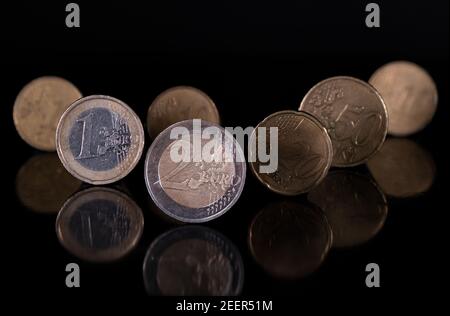 Euro-Münzen stehen auf dem Rand isoliert mit pechschwarzem Hintergrund, reflektierend in schwarz metallischen Oberfläche. Geld auf einem sehr dunklen Tisch. Stockfoto