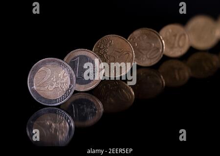 Euro-Münzen stehen auf dem Rand isoliert mit pechschwarzem Hintergrund, reflektierend in schwarz metallischen Oberfläche. Geld auf einem sehr dunklen Tisch. Stockfoto