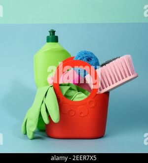 Korb mit Waschschwämmen, Gummischutzhandschuhen, Bürsten und Reinigungsmittel in einer grünen Kunststoffflasche auf blauem Hintergrund, Set Stockfoto