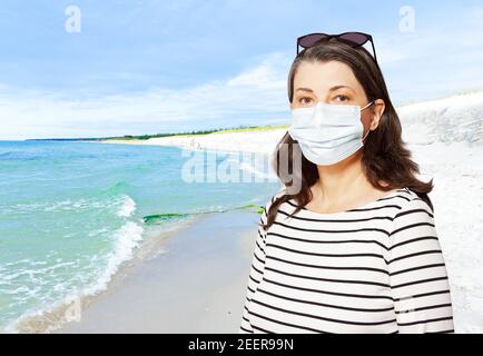 Reisen während der Coronavirus-Pandemie: Frau Tourist mit einer Sonnenbrille und medizinische Gesichtsmaske, vor einem Strand. Stockfoto