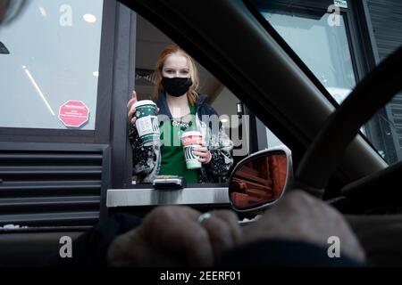Ein maskierter Starbucks Barista, der einem Gast während der Pandemie von Covid durch das Drive-Thru-Fenster Kaffee überreicht. St. Paul Minnesota, USA Stockfoto