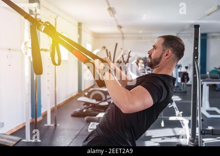Junger Mann, der TRX-Übungen im Fitnessstudio macht. TRX-Schulung Stockfoto