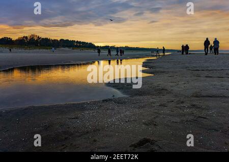 Leute, die am Strand um Pfütze am Wasser über der Ostsee spazieren Meer in Swinoujscie bei Sonnenuntergang im november Stockfoto