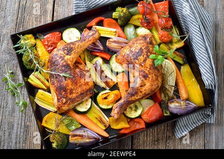 Zwei knusprig gebratene Hähnchenschenkel auf buntem mediterranem Gemüse Heiß serviert auf dem Backblech Stockfoto