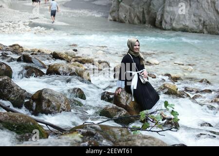 Junge muslimische Frau sitzt auf Stein am Bergfluss. Stockfoto