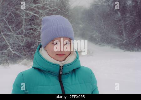 Portrait von schönen Mädchen Teenager 15 Jahre alt im Winterwald. Schneefall im Vordergrund, Bäume mit Reif bedeckt. Warme Kleidung für Winterspaziergang. Stockfoto