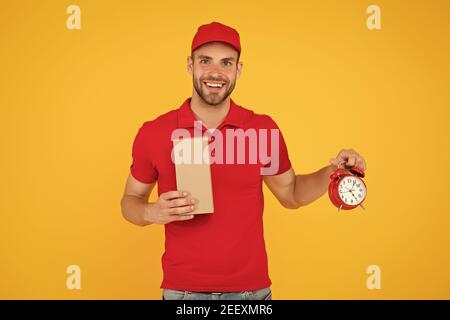 Echte Freude. Gehen Sie online einkaufen. Lieferung während der Quarantäne. Freundliche Mitarbeiter Mann. Lieferzeit. Lieferung Kurier mit Zeit Uhr Haltekasten. Nehmen Sie Ihr Paket. Geschenk Lieferung Mann mit Vintage Uhr. Stockfoto