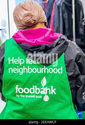 Ein Trussell Trust Foodbank Freiwilliger trägt eine grüne Schürze. Eine asiatische Frau mit Kopftuch, die sich freiwillig für die Bekämpfung der Lebensmittelarmut in London engagiert. VEREINIGTES KÖNIGREICH Stockfoto