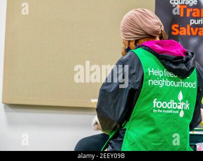 Ein Trussell Trust Foodbank Freiwilliger trägt eine grüne Schürze. Eine asiatische Frau mit Kopftuch, die sich freiwillig für die Bekämpfung der Lebensmittelarmut in London engagiert. VEREINIGTES KÖNIGREICH Stockfoto