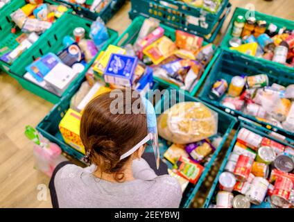 Eine Frau Freiwilligenarbeit bei einer Trussell Trust foodbank Sorts & Sammelt gespendete Lebensmittel aus Kisten, um sie an Kunden zu geben Erleben Sie Lebensmittelarmut in Großbritannien Stockfoto