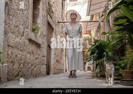 Schöne blonde junge weibliche Reisende tragen Stroh Sonnenhut Sightseeing und genießen Sie Sommerurlaub in einer alten traditionellen Küstenstadt an der Adria