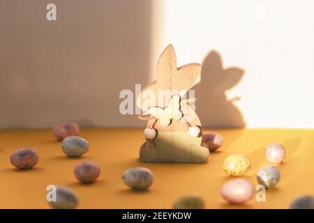 Bemalte Ostereier und Holzspielzeug Kaninchen auf gelbem Tisch mit Schatten. Vorderansicht Stockfoto