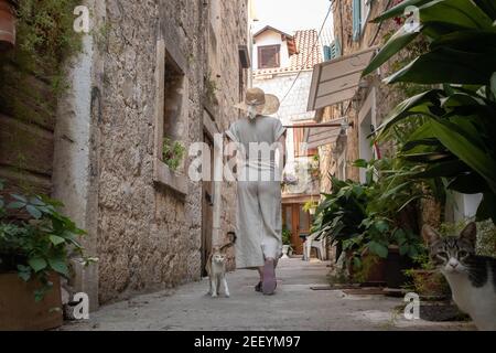 Rückansicht der schönen blonden jungen weiblichen Reisenden tragen Stroh Sonnenhut Sightseeing und genießen Sommerurlaub in einer alten traditionellen Küstenstadt Stockfoto