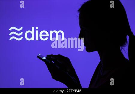 Silhouette eines Mädchens mit Smartphone und Facebook Diem Kryptowährung Logo auf dem verschwommenen Bildschirm. Echtes Foto, keine Montage, keine Nachbearbeitung. Stafford Stockfoto