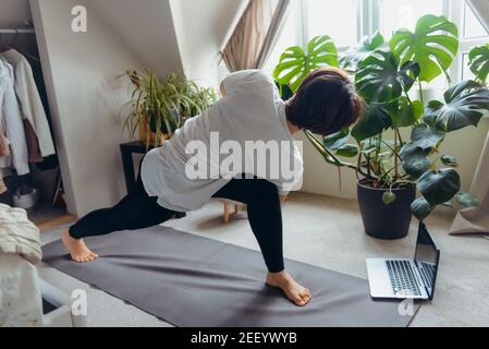 Eine Frau auf einer Matte macht Twist und Stretching Asana Position in ihrem Schlafzimmer. Online-Kurs Yoga zu Hause üben. Gesunder Lebensstil. Online-Training zu Hause Stockfoto