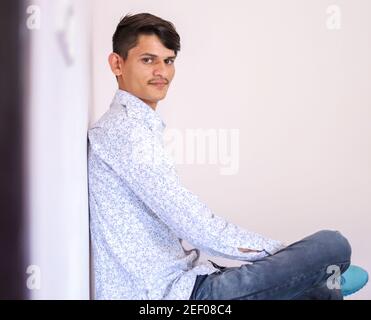 Junger lächelnder indischer Mann sitzt und schaut auf die Kamera Stockfoto