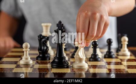 Ein kaukasischer Junge hält während eines Spiels ein weißes Ritterschach in der Hand. Er wird einen Schritt machen. Dunkles Hintergrundbild für Bestimmung, Konzentration, Fokus Stockfoto