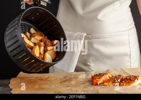 Eine kaukasische Köchin dumpt frisch gebackene Bratkartoffeln Brocken auf einem Stück Backpapier, das drei hat Im Ofen geröstetes mariniertes Lachsfilet mit Stockfoto