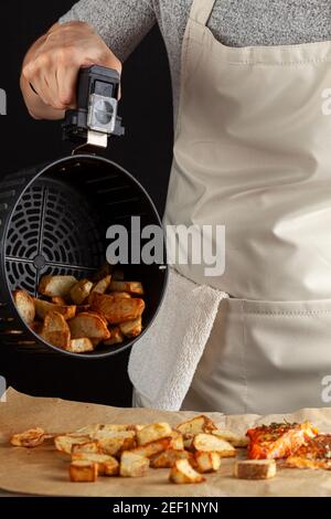 Eine kaukasische Köchin dumpt frisch gebackene Bratkartoffeln Brocken auf einem Stück Backpapier, das drei hat Im Ofen geröstetes mariniertes Lachsfilet mit Stockfoto