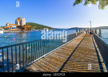 Ein kleiner Junge lehnt sich am Nachmittag über den Dock-Rand An einem Holzdock am See mit einem Hotelresort und Mountain Behind in Coeur d'Alene Idaho USA Stockfoto