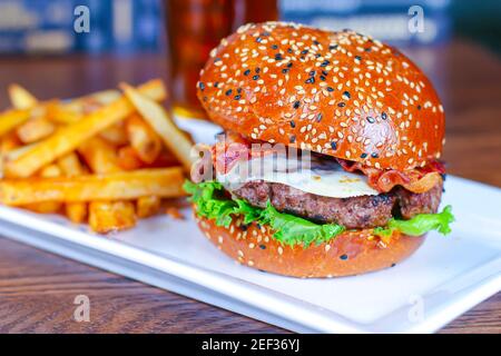 Ein Käse, Bacon Hamburger mit pommes auf einem weißen Teller. Stockfoto