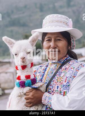 YANQUE, COLCA VALLEY, PERU - 20. JANUAR 2018: Die gebürtige Frau posiert für ein Porträt mit einem Baby Alpaka mit typischen Kostüm in der traditionellen Colca V Stockfoto