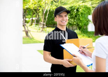 Lächelnder Lieferer in schwarzer Uniform, der Paketboxen zu uns bringt Eine Frau Stockfoto