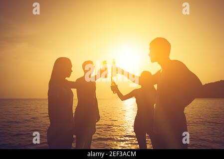 Silhouette von Leuten, die Party machen, Bierflaschen klatschen, beim Sonnenuntergang am Strand anstoßen Stockfoto