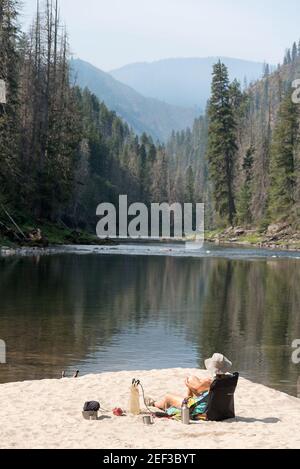 Frau Rucksacktouristin, die sich an einem Strand entlang des Selway River, Idaho, entspannt. Stockfoto