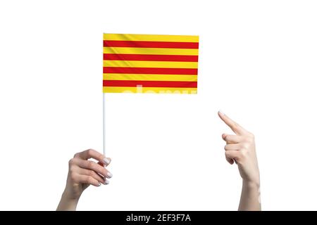 Eine schöne weibliche Hand hält eine katalanische Flagge, auf der sie den Finger ihrer anderen Hand zeigt, isoliert auf weißem Hintergrund. Stockfoto