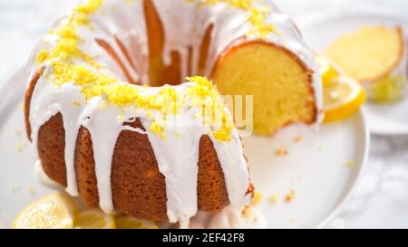 Schritt für Schritt. Schneiden von Zitronenbundtkuchen mit Zitronenschale auf einem Kuchenständer verziert. Stockfoto