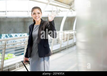 Junge asiatische Geschäftsfrau mit Gepäck winken Hand bye auf Der Flughafen - Geschäftsreisekonzept Stockfoto