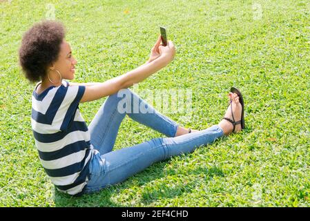 Junge Casual afro Frau auf dem Gras sitzen Selfie Stockfoto
