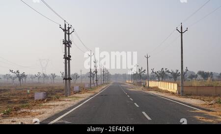 10. Februar 2021- Sikar, Jaipur, Indien. Schwarze lange Asphaltstraße durch Strommasten. Lange Pflasterstraße Nahaufnahme endet am Horizont. Stockfoto