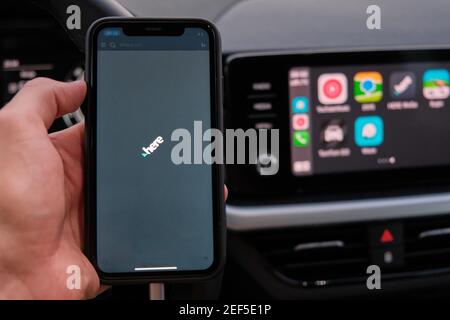 Hier App auf dem Bildschirm des Smartphones in mans Hand auf dem Hintergrund des Auto-Dashboard-Bildschirm mit Anwendung Von Navigation oder Karten von Apple Car Stockfoto