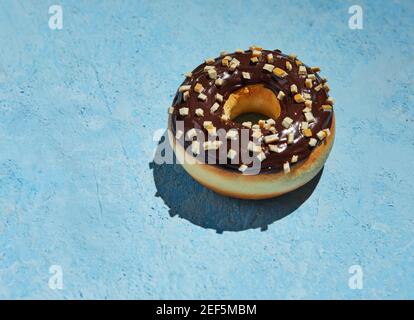 Donut mit Schokoladenzuckerguss und Streuseln auf blauem Hintergrund. Stockfoto