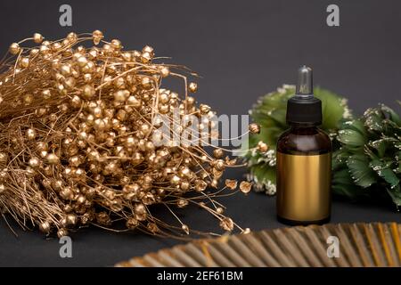 Goldene Glasflasche mit Kosmetik auf schwarzem Hintergrund mit Bouquet von goldgetrockneten Blumen. Tropf mit kosmetischem Öl oder Serum. Anti-Aging-Gesichtsbehandlung Stockfoto