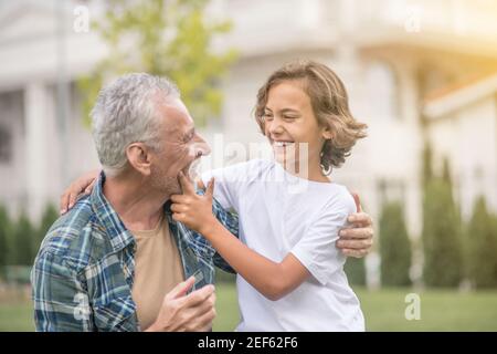 Grauhaariger Mann umarmt seinen Sohn und sieht glücklich aus Stockfoto