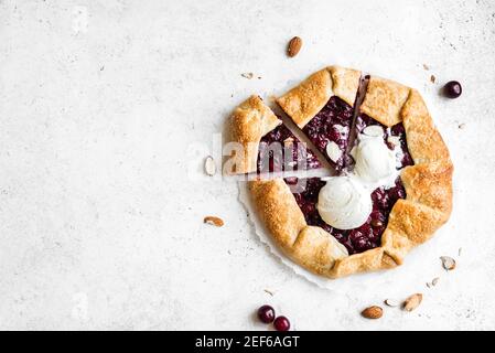 Kirschgalette mit Mandeln und Vanilleeis auf weißem Tisch, Draufsicht, Kopierraum. Hausgemachte gesunde Dessert - Kirschkuchen oder französisch Galette. Stockfoto