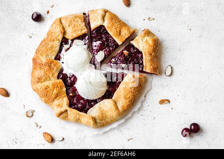 Kirschgalette mit Mandeln und Vanilleeis auf weißem Tisch, Draufsicht, Kopierraum. Hausgemachte gesunde Dessert - Kirschkuchen oder französisch Galette. Stockfoto