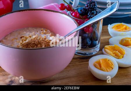 Eine Schüssel mit Brei serviert mit gekochten Eiern und frisch Beeren Stockfoto