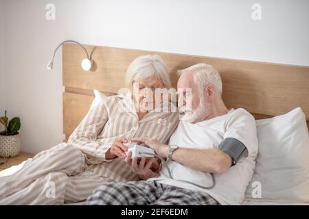 Grauhaariger älterer Mann, der zusammen mit seinem Blutdruck überprüft Frau Stockfoto