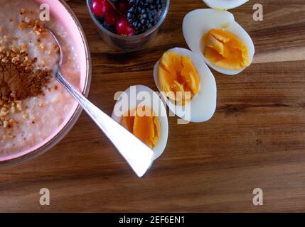 Gesundes Frühstück mit Hirsebrei, Nüssen mit frischen Beeren und gekochten Eiern auf Holzgrund mit Kopierplatz serviert Stockfoto