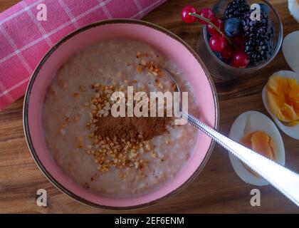 Eine Schüssel mit frisch gekochtem Brei mit gerösteten Mandeln und Zimt serviert mit einem Glas frische Beeren und gekocht Eier Stockfoto