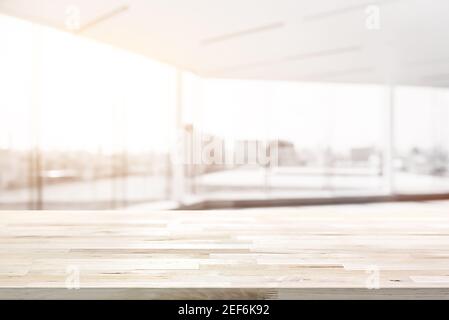 Holztischplatte in verschwommenem weißen Bürozimmer mit Glaswand und Blick auf das Stadtgebäude im Hintergrund - CAN Für die Anzeige oder Montage Ihrer Produkte verwendet werden Stockfoto